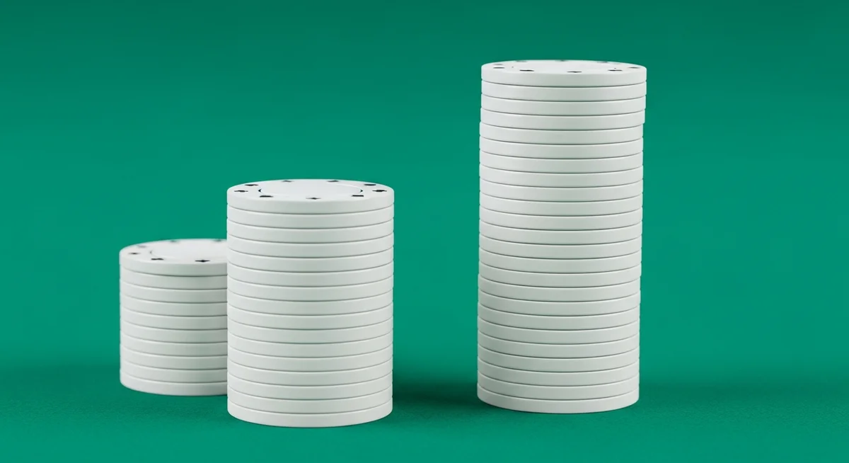 A small stack of plain casino chips next to a much taller stack of plain casino chips on a deep green baize surface.