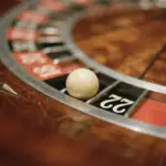 A white roulette ball rests in the number 22 slot on a wooden roulette wheel