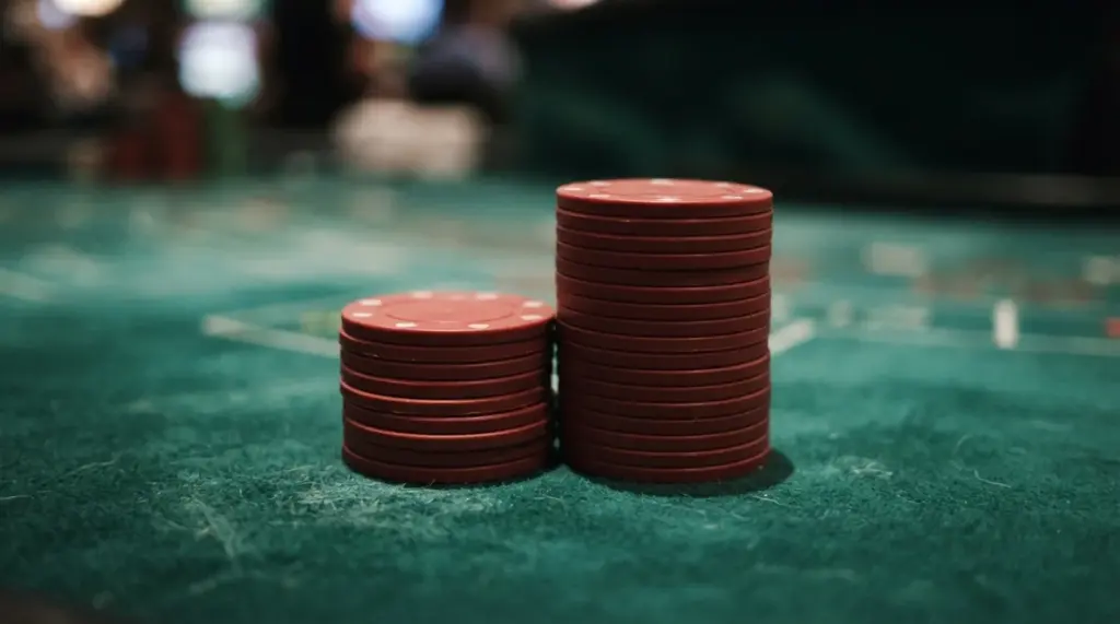 Two stacks of red gambling chips sit on a green felt table surface