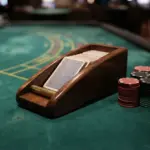 A close-up, eye-level photograph of a polished wooden card shoe resting squarely on deep green baccarat baize
