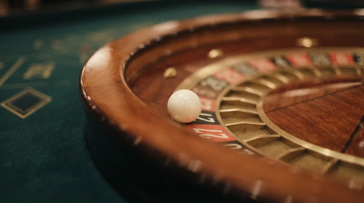 A white roulette ball rests on the number 27 inside a wooden roulette wheel on a green felt table