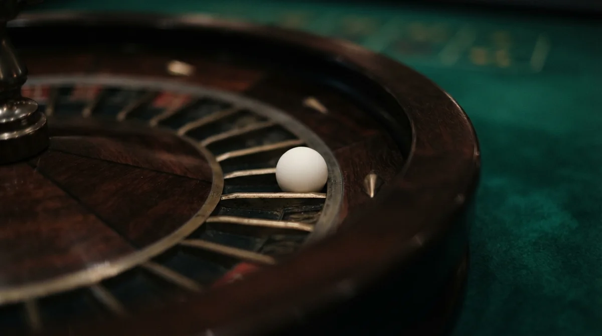 A white ball rests in a slot of a dark wood roulette wheel on a green felt table