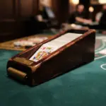 A wooden blackjack dealing shoe holding a deck of cards on a green casino table