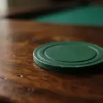 A single, plain deep green casino chip resting perfectly flat on a rich, polished warm wood surface