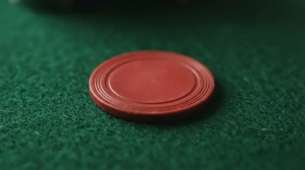 A plain red circular gaming chip rests on a green felt surface