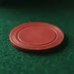 A plain red circular gaming chip rests on a green felt surface