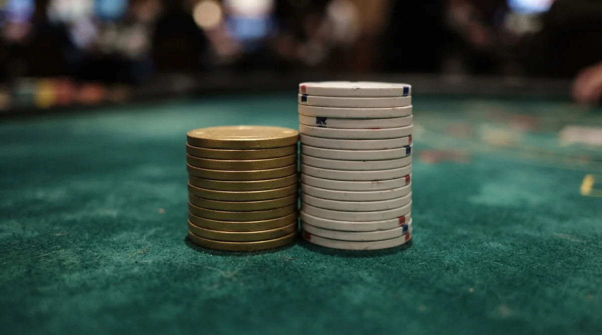 Two stacks of poker chips, one gold and one white, sit on a green felt casino table