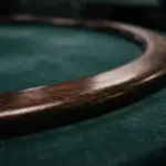 A close-up photograph of an empty dark wood poker table rail resting on deep green baize